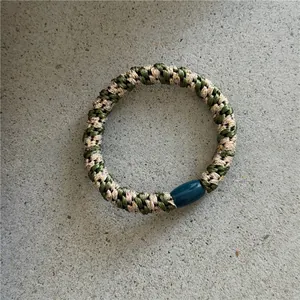 Détail d'un élastique à cheveux tressé vert et or avec une boucle en résine bleue