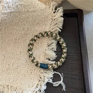 Détail d'un élastique tressé avec fils vert et or et un curseur en perle bleue