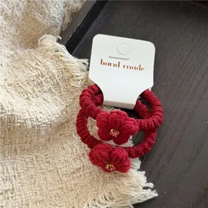 Nahaufnahme handgemachter dunkelroter Strickblumen-Haargummis mit lila Strass-Zentrum