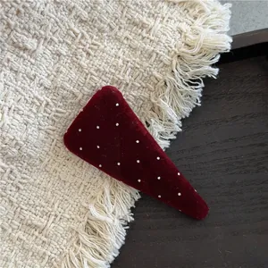 Close-up of a burgundy velvet triangular hair clip with white polka dots on a wooden plate