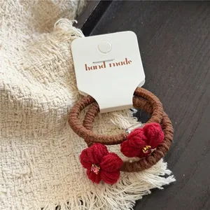 Detailansicht handgefertigter roter Strickblumen-Haargummis mit rosa Strass auf weißer Karte
