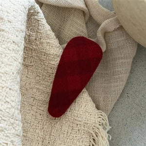Close-up of a red checkered fabric hair clip on a white knit fringe background