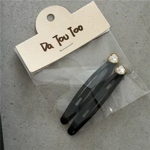 Detalle de dos pinzas para el cabello con pedrería de corazón en tarjeta de cartón
