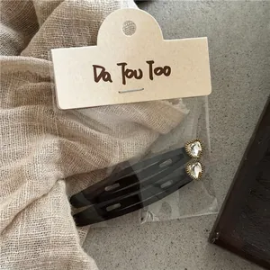 Detalle de dos pinzas para el cabello negras con corazones de strass en tarjeta
