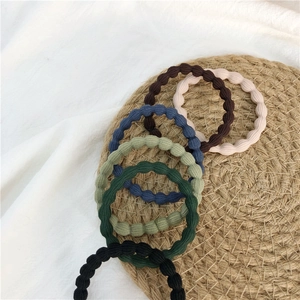 Detail of high-elasticity wave textured hair ties in dark colors on a woven mat