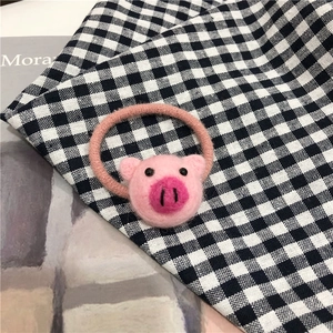 Dettaglio di un elastico per capelli a forma di maialino rosa in lana feltro su tessuto