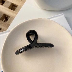 Gros plan d'une pince à cheveux torsadée noire brillante sur une assiette en céramique
