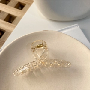 Vue détaillée d'une pince à cheveux transparente champagne avec ressort doré sur plat céramique