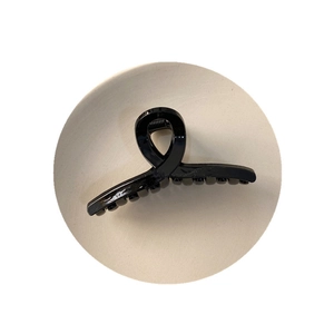 Pince à cheveux torsadée noire brillante sur un plateau rond minimaliste crème