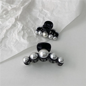 Detail of black glossy resin hair claws with elegant faux pearl embellishments