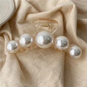 Close-up of elegant amber hair claw clip with five white gradient pearls on linen