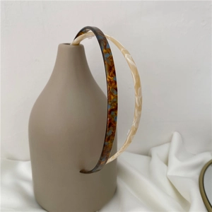 Minimalist tortoiseshell and marble acetate headbands set on a ceramic vase
