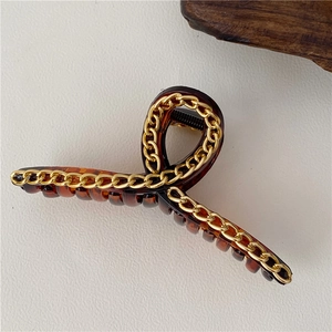 Dettaglio di un grande fermaglio per capelli in resina ambrata con catena dorata e design