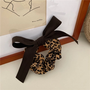 Detailed close-up of a brown bow leopard print scrunchie on an artistic white background