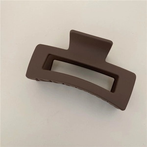 Top view of a matte coffee brown rectangular hollow hair claw clip on a beige background