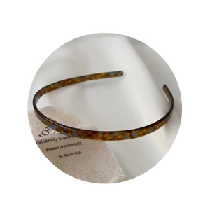 Elegant tortoiseshell acetate headband with blue spots on a soft fabric background