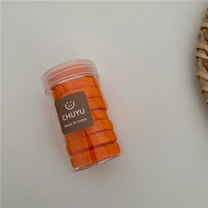Detail of orange elastic hair ties in a clear cylindrical jar with a branded logo label