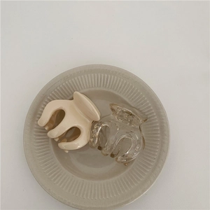 Detail of cream and transparent mini shark hair clips on a textured ceramic tray