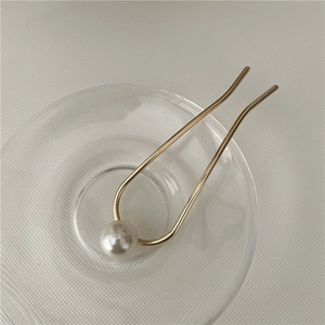 Macro detail of a minimalist gold U-shaped hairpin with a large pearl in a glass tray