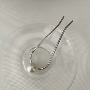 Macro detail of U-shaped silver hair pin with a single large white pearl on glass