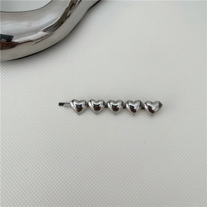 Dettaglio del fermaglio per capelli argento con cinque cuori metallici lucidi su bianco