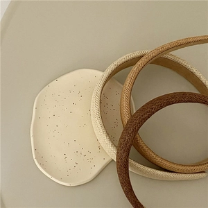 Detail of three woven headbands in cream, beige and brown on a ceramic tray