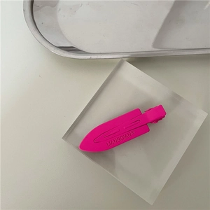 Close-up of matte rose pink metal hair clip with embossed lettering on acrylic block