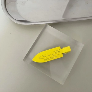 Detail of yellow matte metal duckbill hair clip with embossed brand lettering