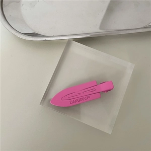 Detail of matte pink alligator hair clip with brand embossing on transparent block