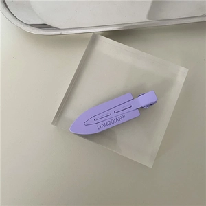 Close-up of a purple matte hair clip with brand logo on minimalist acrylic display stand