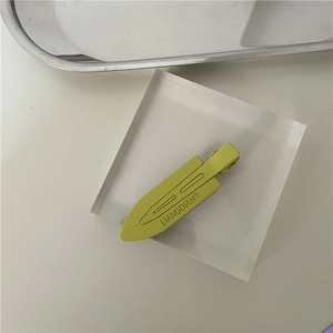 Detail view of a matte lime green metal hair clip on a minimalist acrylic stand