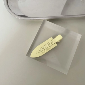 Detail view of a pale yellow matte metal hair clip on a transparent acrylic block