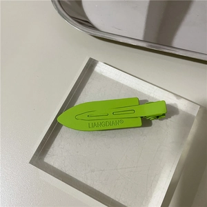 Detail view of a lime green matte styling hair clip resting on a clear acrylic block