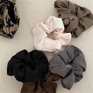Detail showing five assorted earth-tone satin scrunchies in silk-like pleated fabric