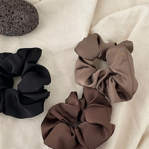Close-up of three satin scrunchies in black and brown shades on textured fabric
