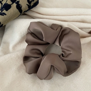 Close-up of deep brown satin scrunchie with layered folds on ivory textured fabric