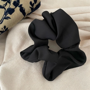 Close-up of black satin scrunchie with soft pleats on rustic linen fabric background