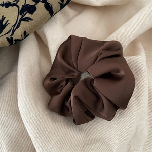 Close-up of a brown satin scrunchie showing smooth texture and elegant pleated details