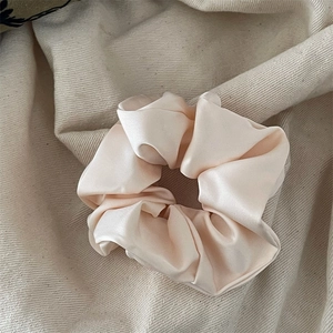 Detail shot of a soft champagne pink satin scrunchie with elegant pleated fabric texture