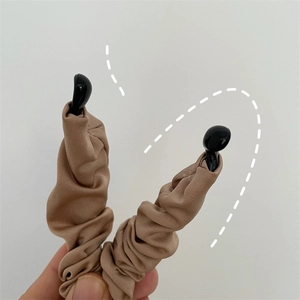 Detail showing elastic light brown pleated fabric hair clip with glossy black resin ends