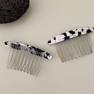 Detail view of two acetate hair side combs with black and white marble cow pattern texture
