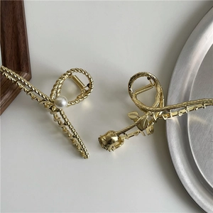 Detailed close-up of golden metallic rose and pearl hair claw clips with elegant textures