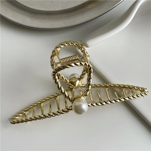 Detailed view of a gold hair claw clip featuring a braided texture and a large white pearl