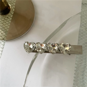 Dettaglio del fermaglio in argento con quattro cristalli a cuore su sfondo a griglia