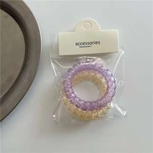 Detalle de gomas de pelo en espiral color púrpura y champán en embalaje transparente