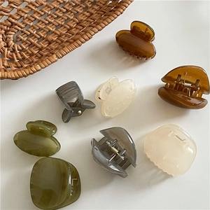 Close-up of assorted geometric resin hair claws in amber and cream on a woven texture