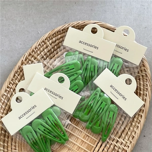 Set de cinq barrettes BB en métal vert crème sur cartes de présentation dans un panier tressé