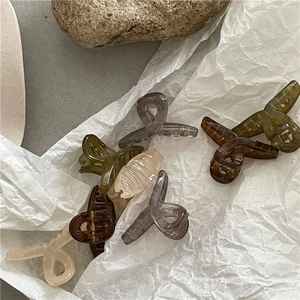 Jelly-colored matte resin hair claws in olive green and amber on a minimal artistic background