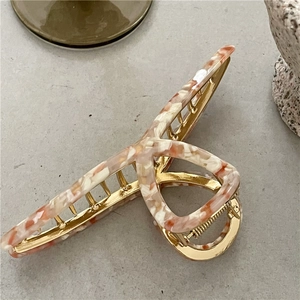 Detail of golden metal hair claw with pink marble acetate pattern and cross design
