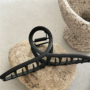 Minimalist black hair claw clip with crossed metal curves on natural stone base